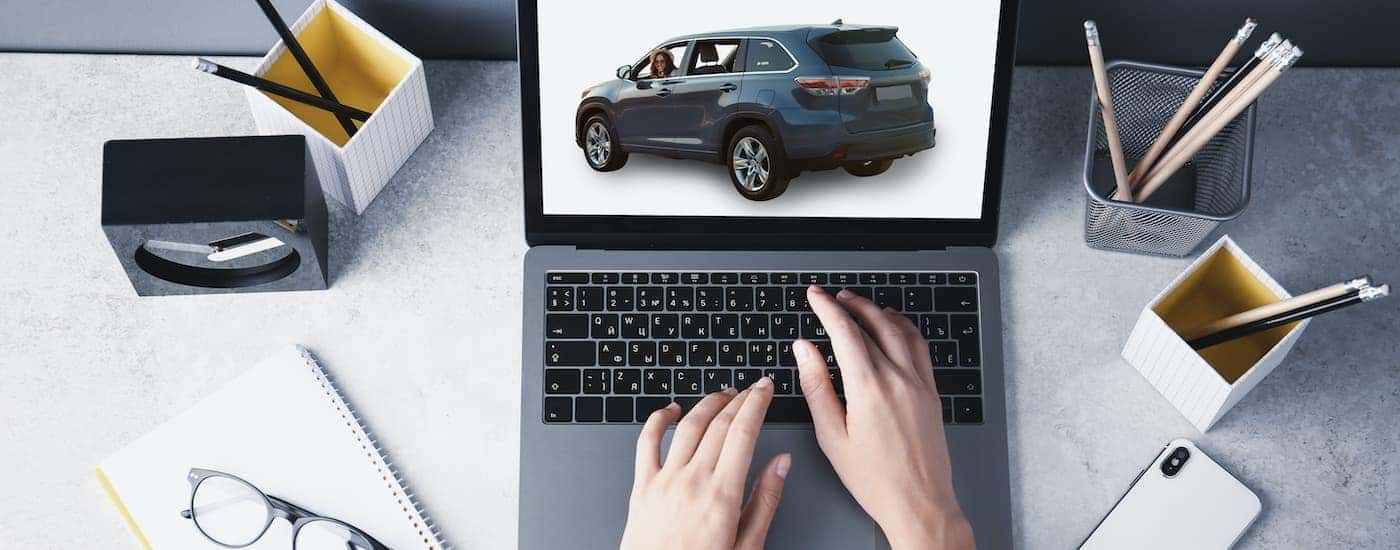 A laptop is shown from a high angle with an SUV on the screen with someone looking to buy a used car online.