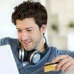 A man is holding his credit card as he enters the information into a computer.