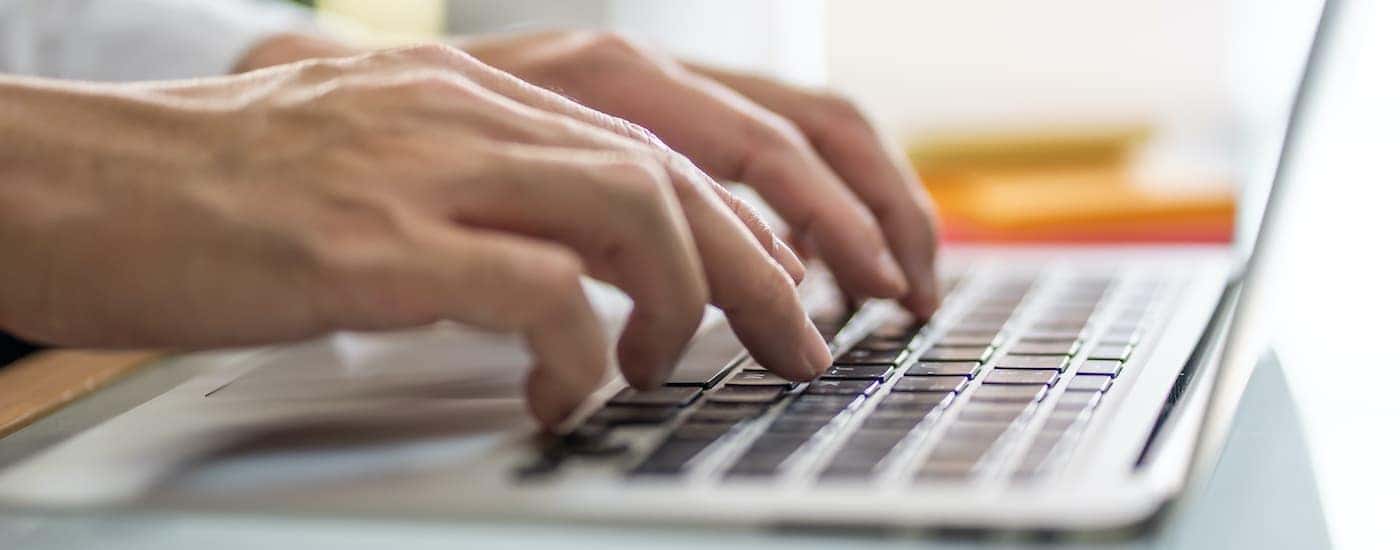 A man is typing "Louisville used car lot," into a computer.