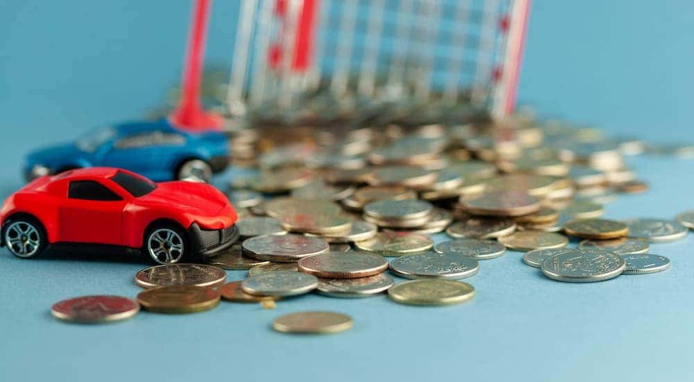 Two toy cars and a toy shopping cart sitting in a pile of change