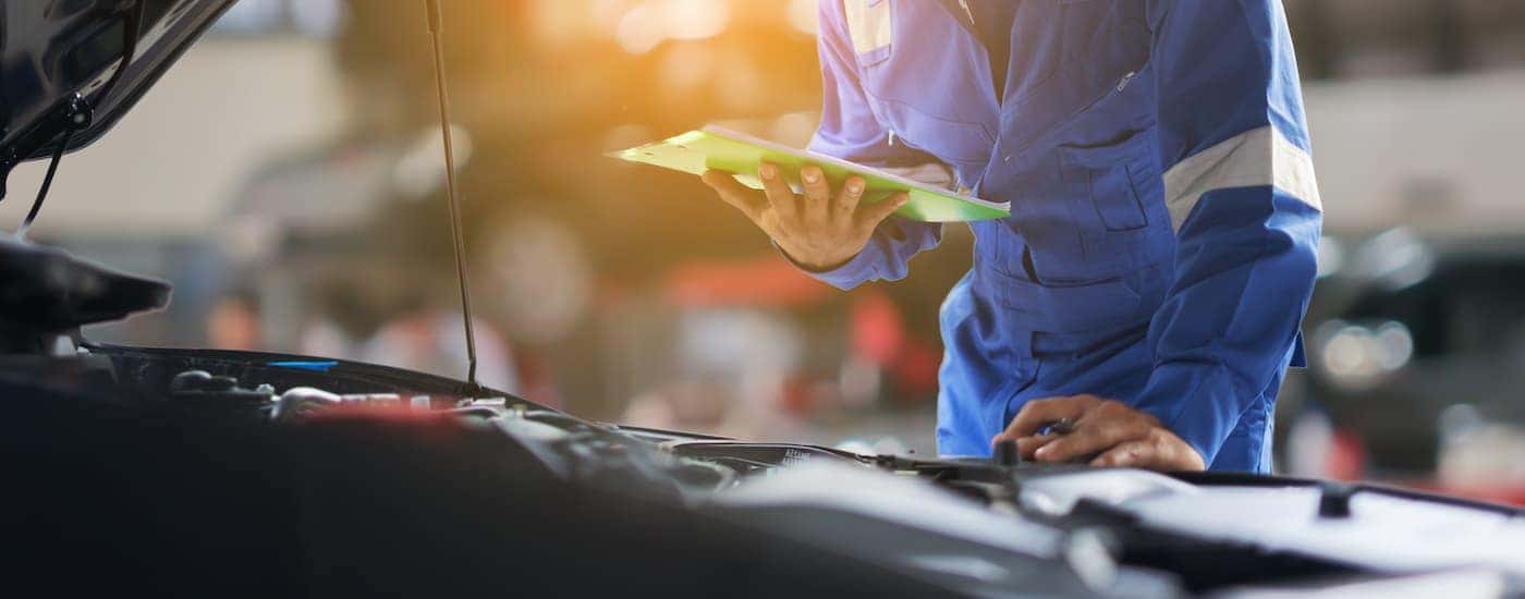 A mechanic with a clipboard is looking at an engine bay.