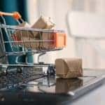 A close up shows a tiny shopping cart parked on a laptop keyboard.