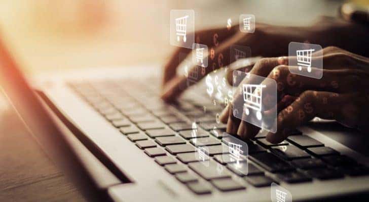 A person is typing on a laptop with floating cart and money icons.