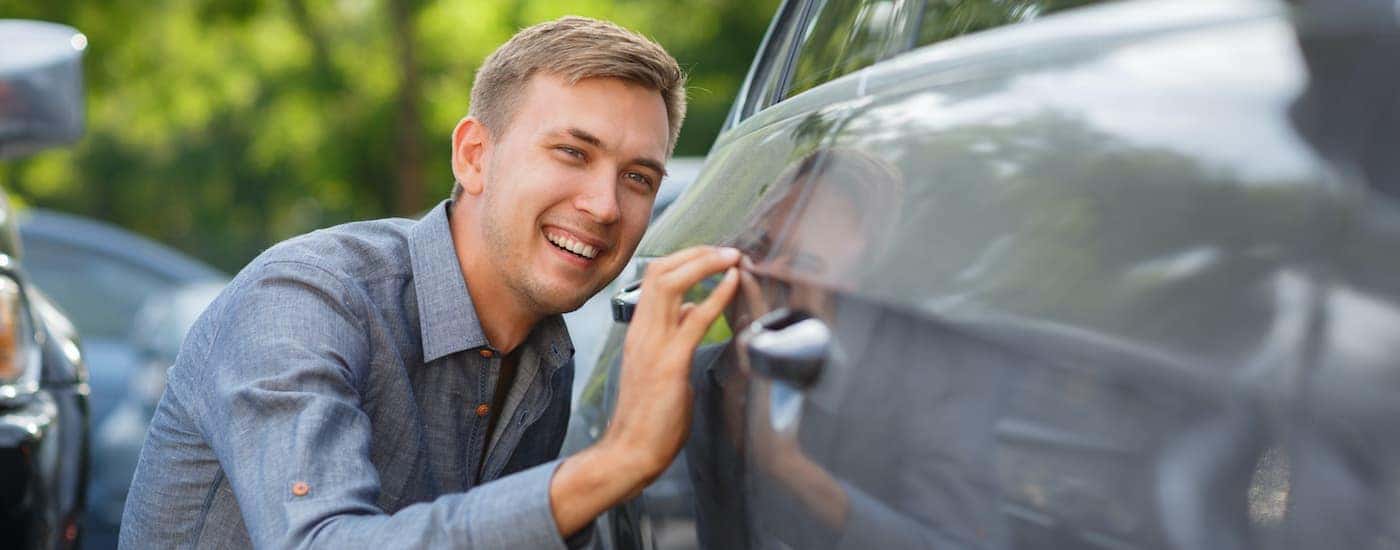 A person is crouching next to a used car for sale.