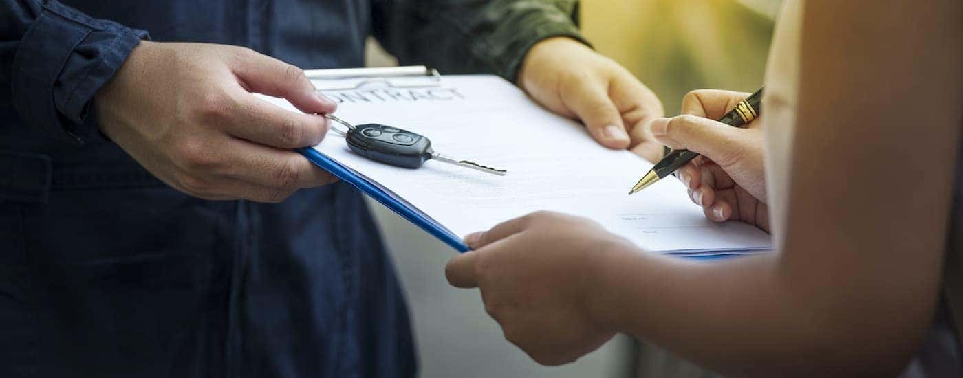 A person is signing paperwork at a used car dealership.