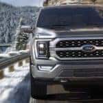 A grey 2020 Ford F-150 is shown driving down a snow lined road.
