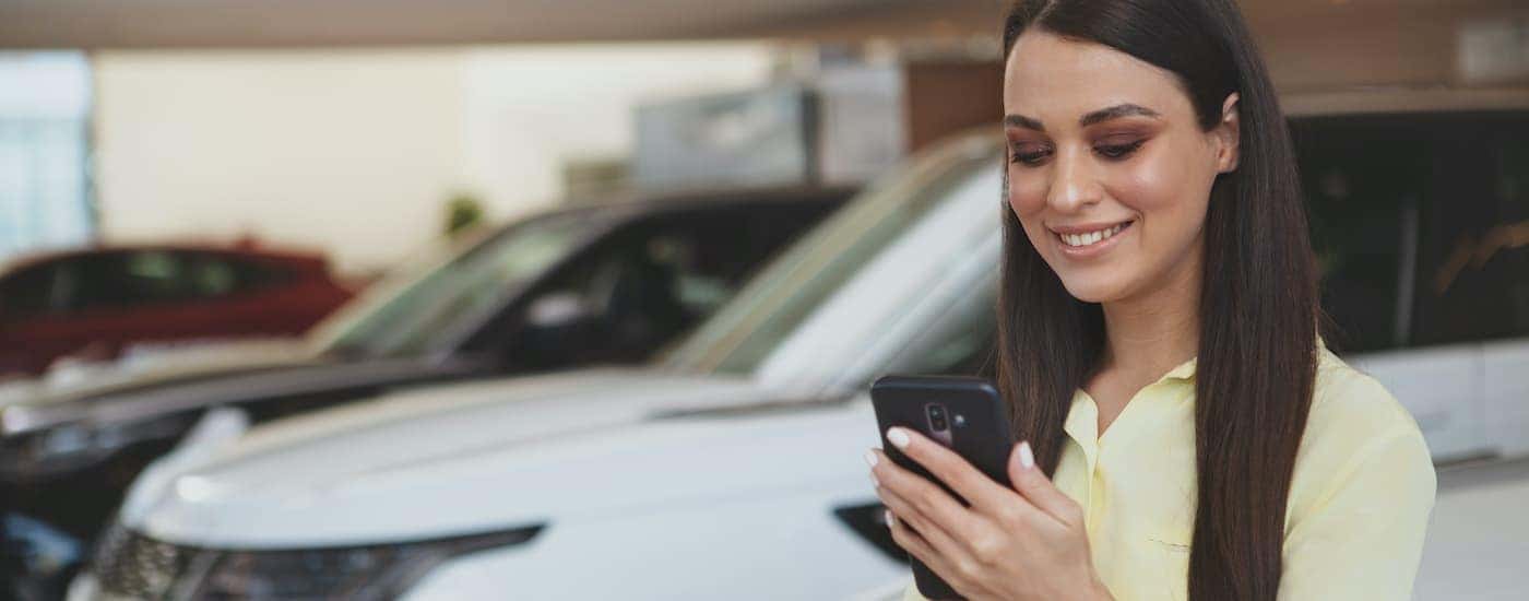 A person is using their cellphone in a car lot to search for Indianapolis online car sales.