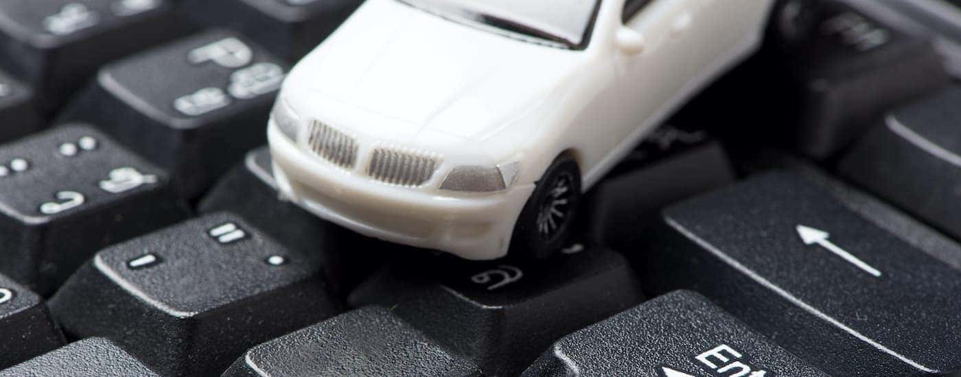 A white toy car is sitting on a keyboard.