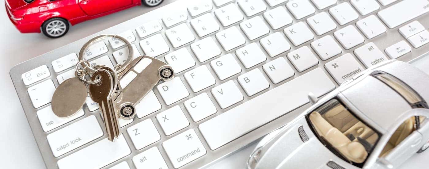 Two toy cars are shown leaning on a white computer keyboard.