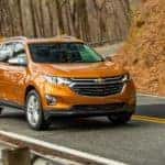 An orange 2018 Chevy Equinox is shown driving on a woodsy road.