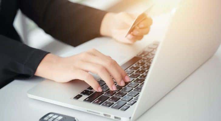 A person is shown typing credit card information into a laptop.