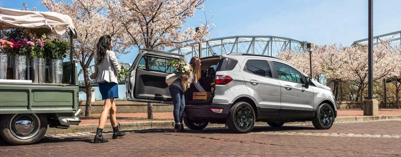 A silver 2020 Ford EcoSport is shown with flowers being loaded into the trunk.