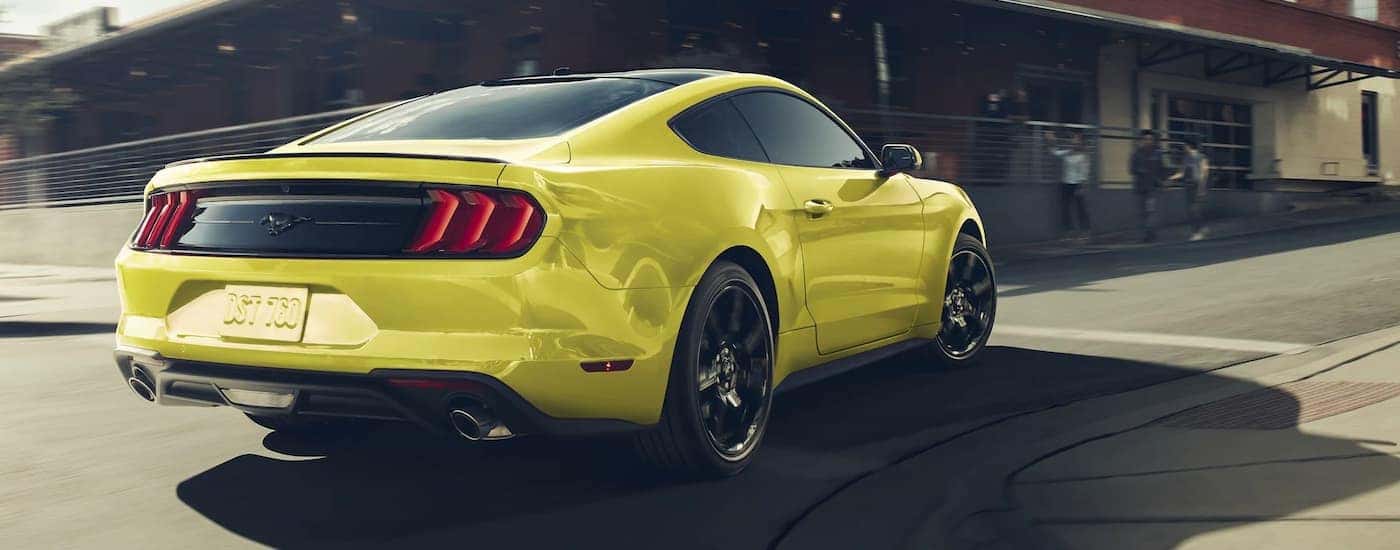 A popular vehicle in Kentucky online car sales, a yellow 2020 Ford Mustang, is shown from behind driving on a city street.