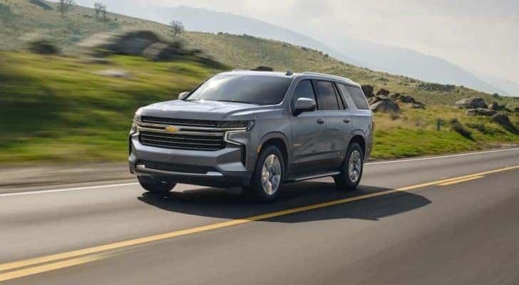 A grey 2021 Chevy Tahoe is shown driving down an empty road.