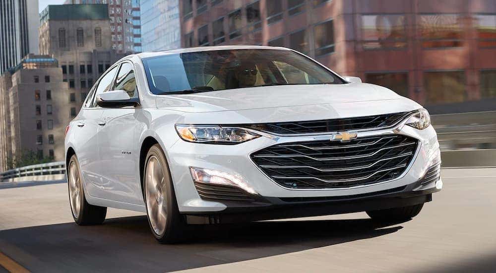 A white 2021 Chevy Malibu is shown driving on a city street.