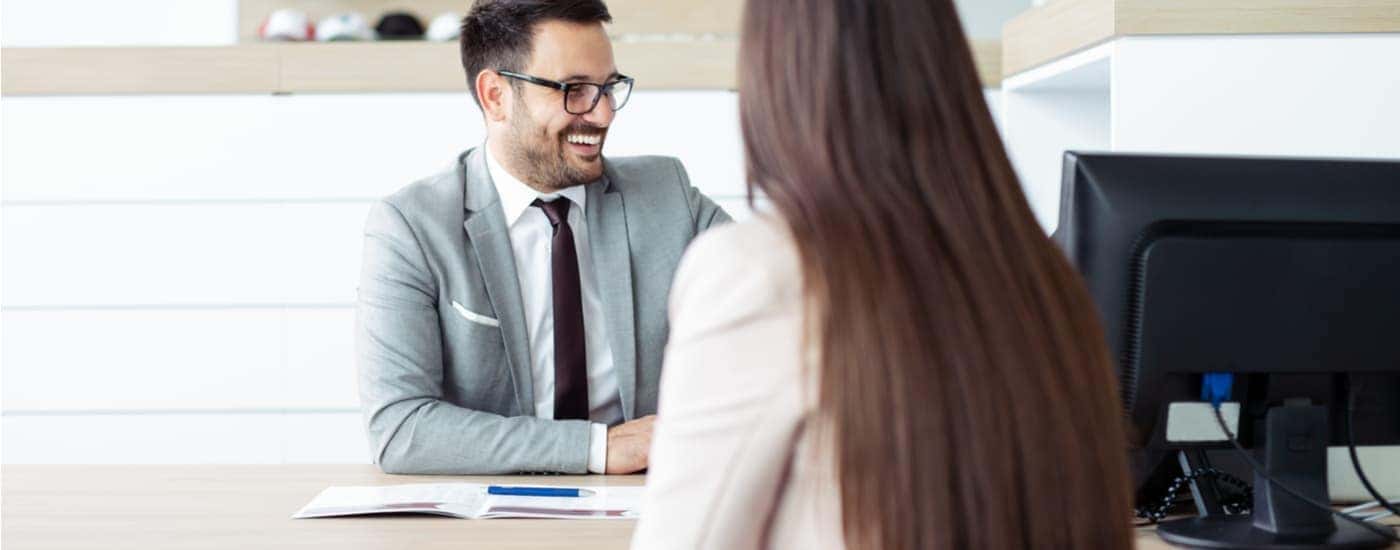 A salesman is shown speaking to customer at a desk.