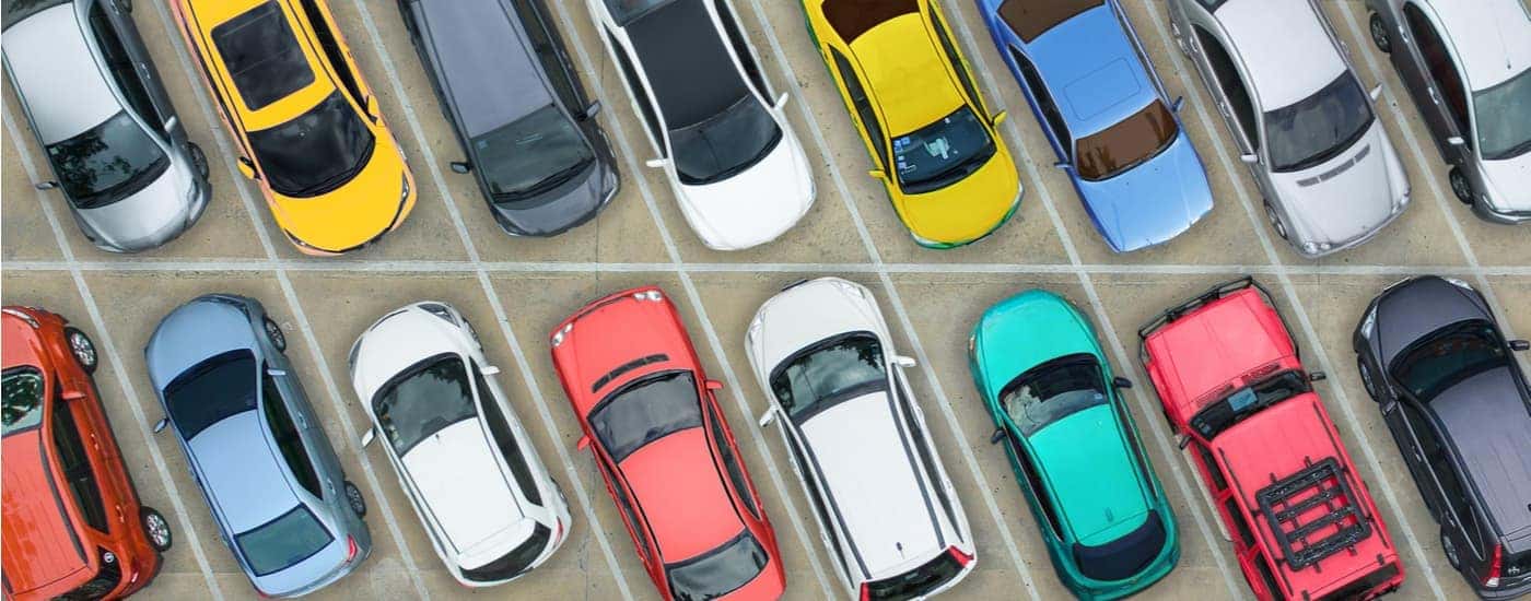Two row of colorful cars are shown in a parking lot.