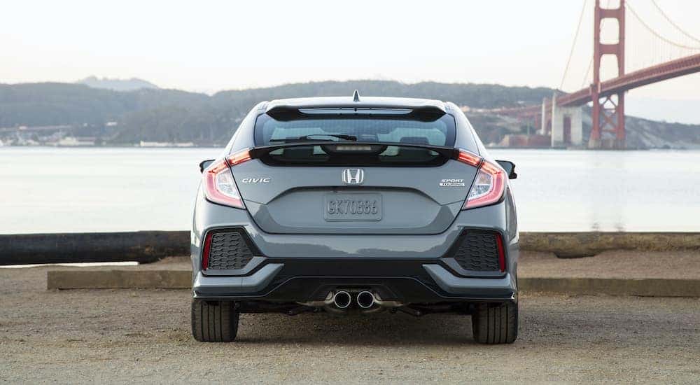 A light blue 2019 Honda Civic Hatchback Sport Touring is shown from the rear parked in front of the San Francisco bridge.