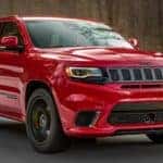 A red 2020 Jeep Grand Cherokee Trackhawk is shown from the front driving on an open road.