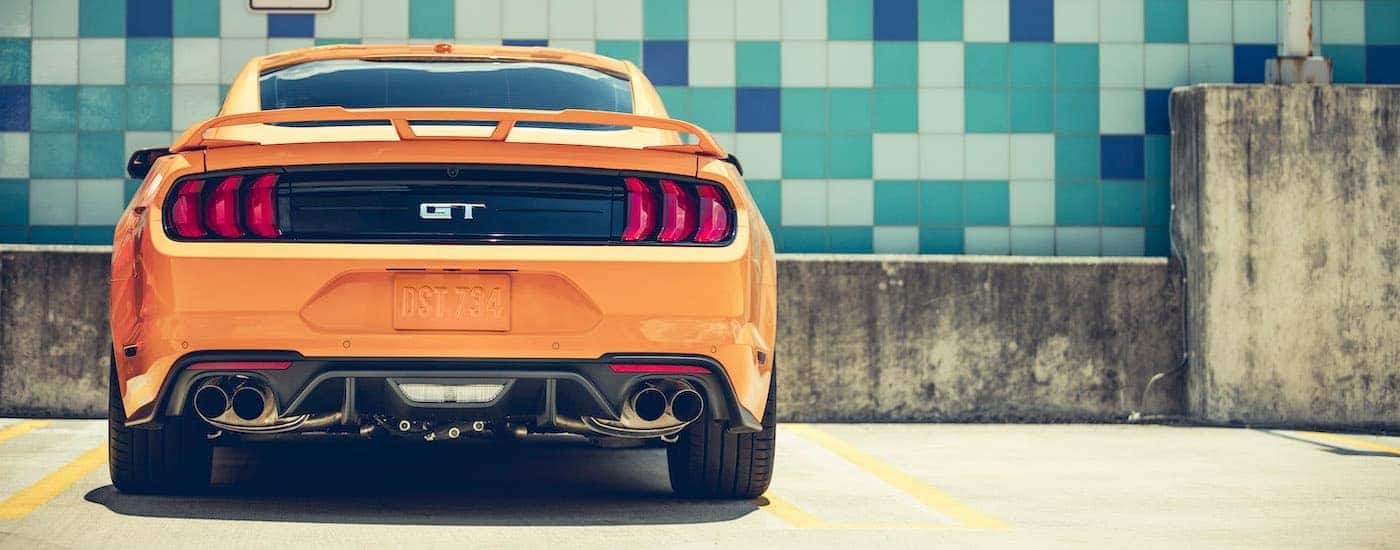 An orange 2018 Ford Mustang GT is shown from behind near a tile wall after visiting an online car dealer in Lawrence Indiana.