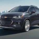 A black 2020 Chevy Trax is shown from the front driving past a city.