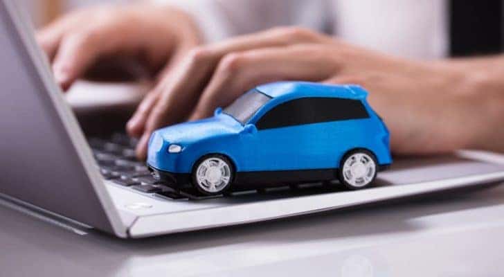 A blue toy car is shown on the keyboard of a laptop.