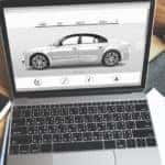 A laptop screen shows a silver sedan on a St Matthews online car sales page.