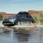A silver 2017 Subaru Outback is shown from the side off-roading through a river.
