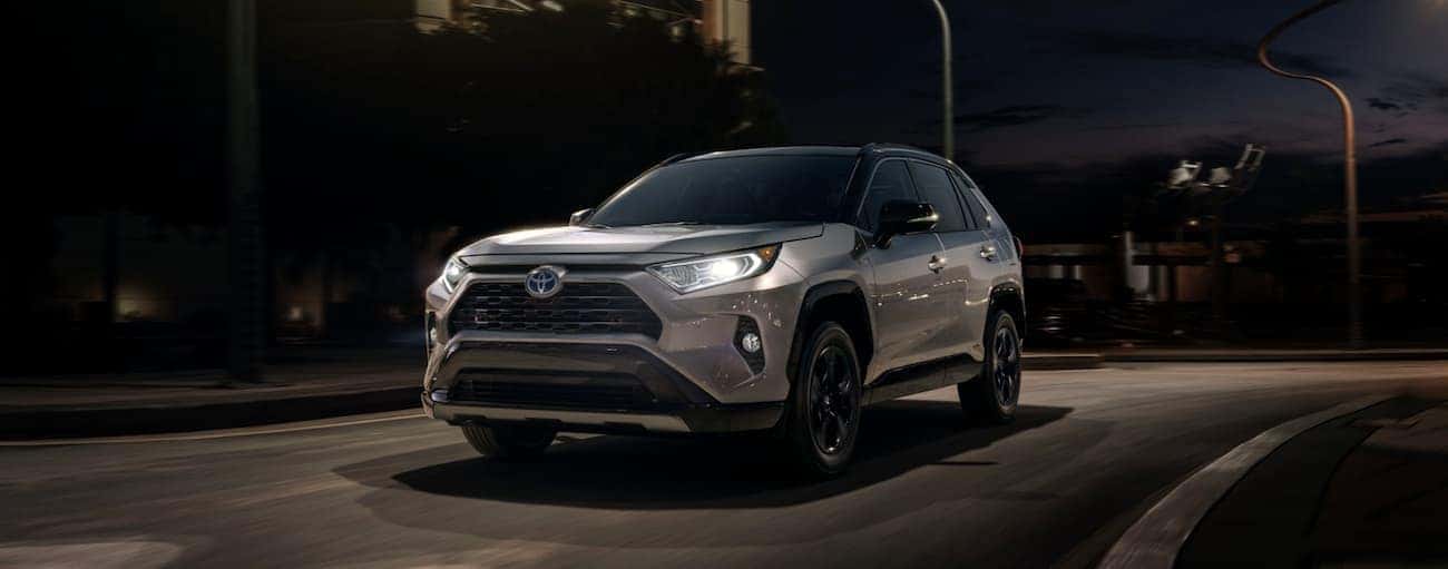 A silver 2020 Toyota RAV4 is shown driving through a city at night.