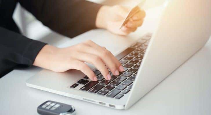 A person is shown typing their credit card information into a laptop after looking at a Reynoldsburg online car dealership.