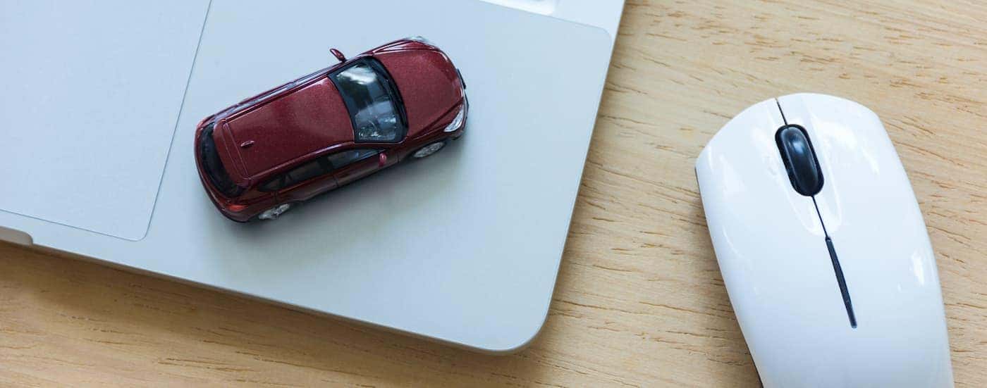 A toy car is shown resting on a laptop next to a computer mouse.