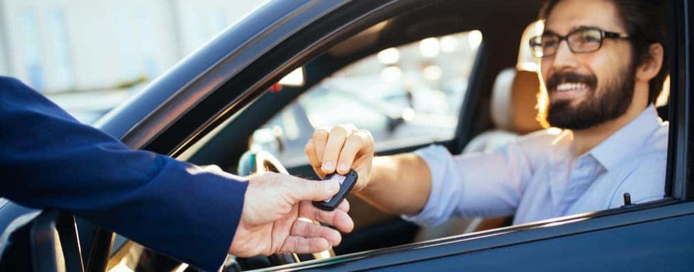 A salesman is shown speaking to a customer sitting inside of a vehicle.