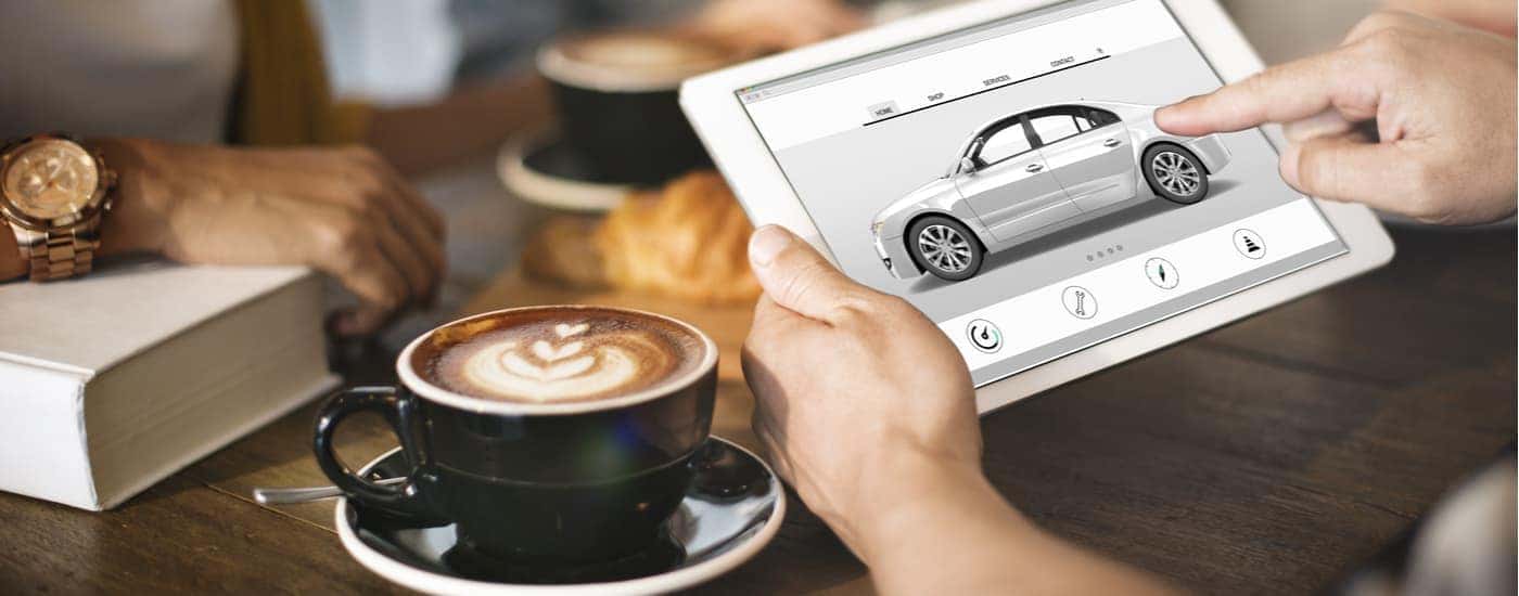 A person is shown researching cars online at a coffee shop.