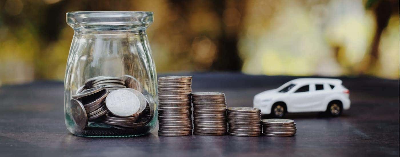 A white toy car is near a glass jar and stack of coins.