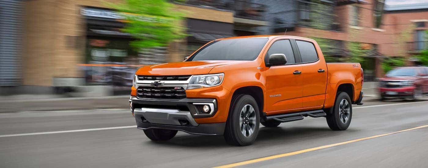 An orange 2021 Chevy Colorado is shown from the front while driving down a city street.