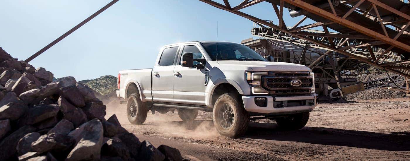 A white 2021 Ford F-250 Super Duty Tremor is shown from the front at an angle while driving through a jobsite.