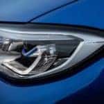 A close up shows the driver side headlight on a blue 2020 BMW 3 Series.