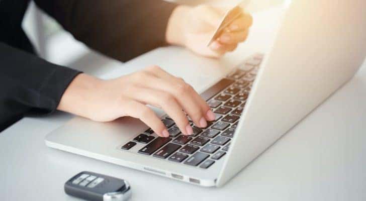 A person is shown typing a credit card number into a laptop.