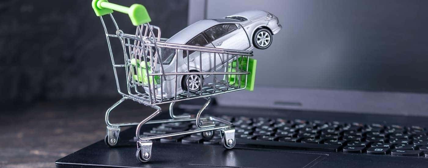 A toy car is shown in a miniature shopping cart on a keyboard.