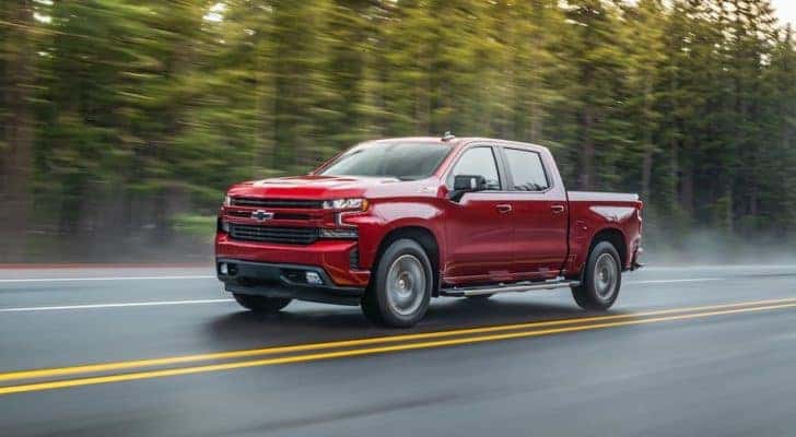 A red 2020 Chevy Silverado 1500 is shown driving on a tree-lined road.