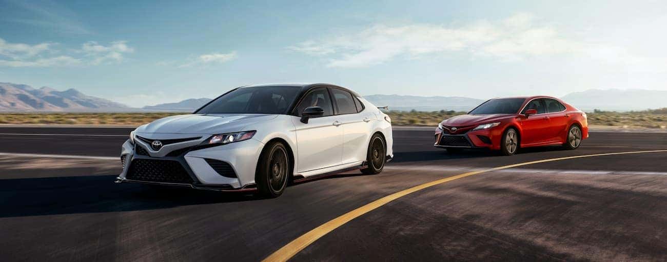 A white and red 2020 Toyota Camry are shown driving on a track.