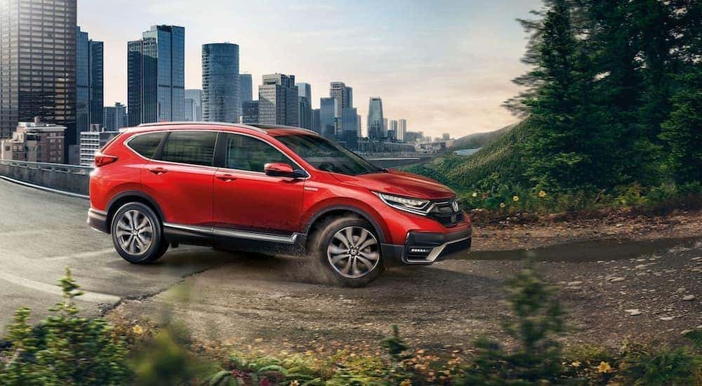 Side view of a red 2020 Honda CR-V driving from the city onto a dirt road