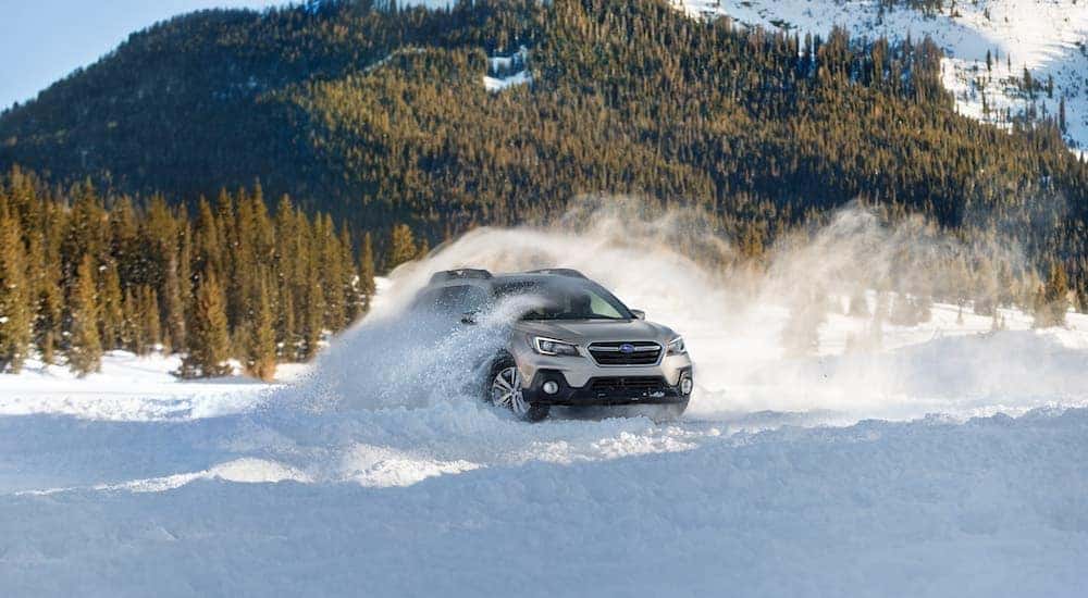 A silver 2019 Subaru Outback is shown driving in the snow after searching online Subaru Outback sales.