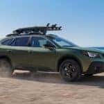 A green 2021 Subaru Outback is shown off-roading on a beach.