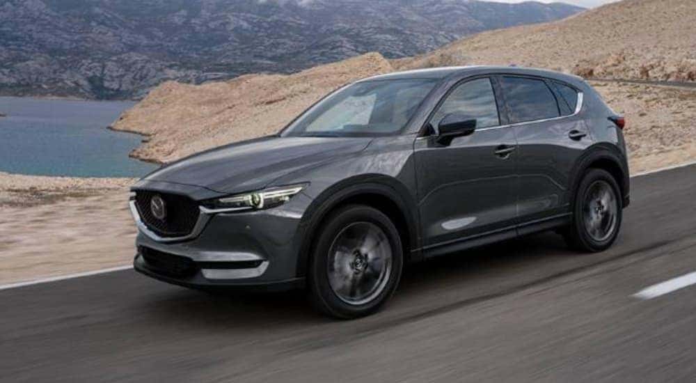 Side view of a grey 2020 Mazda CX-5 driving past water and mountains