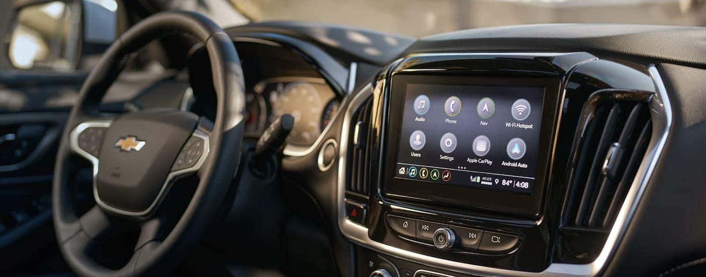 The black interior of a 2023 Chevy Traverse shows the steering wheel and infotainment screen.