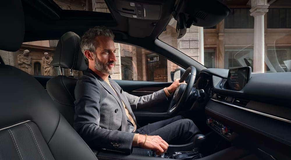 A person is shown driving a 2020 Mazda6 on a city street.
