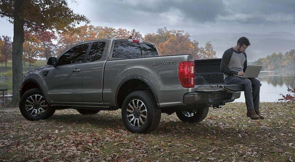 A person is shown online car shopping in the bed of a grey 2022 Ford Ranger Sport.