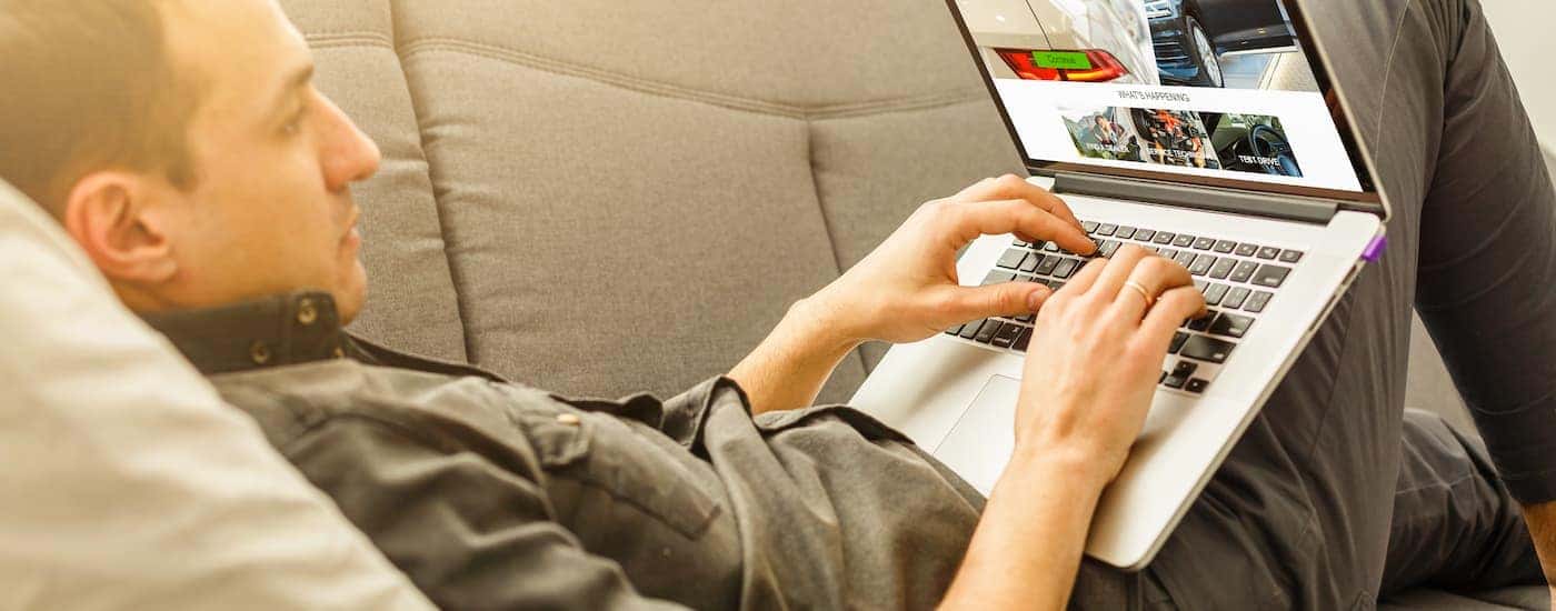 A man is shown using a laptop to search for Cleveland car sales online.