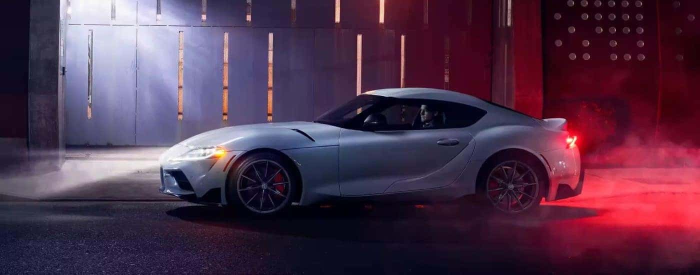 A white 2023 Toyota GR Supra is shown from the side on a city street at night.